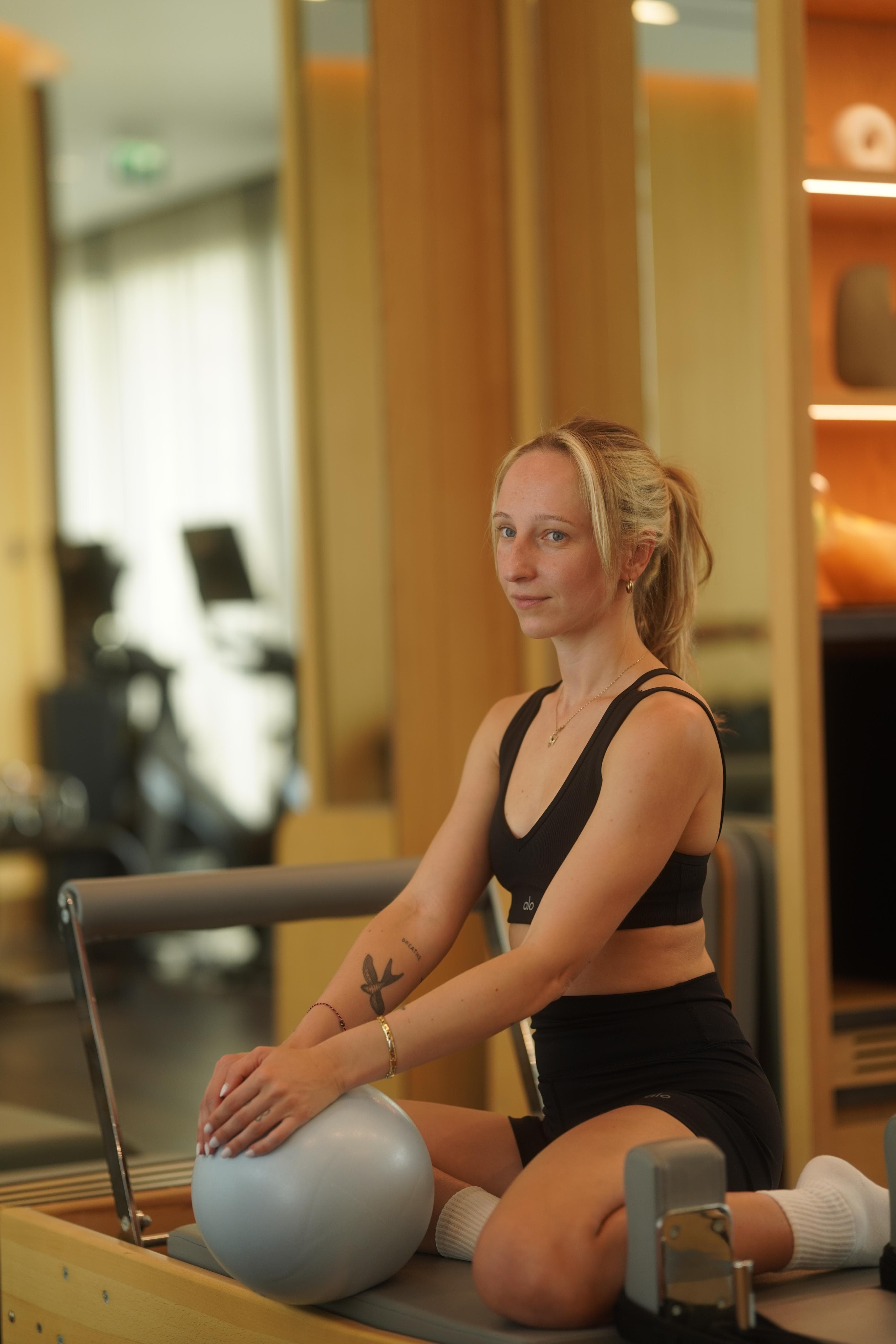 Alexandra, sitting on a reformer with a Pilates ball